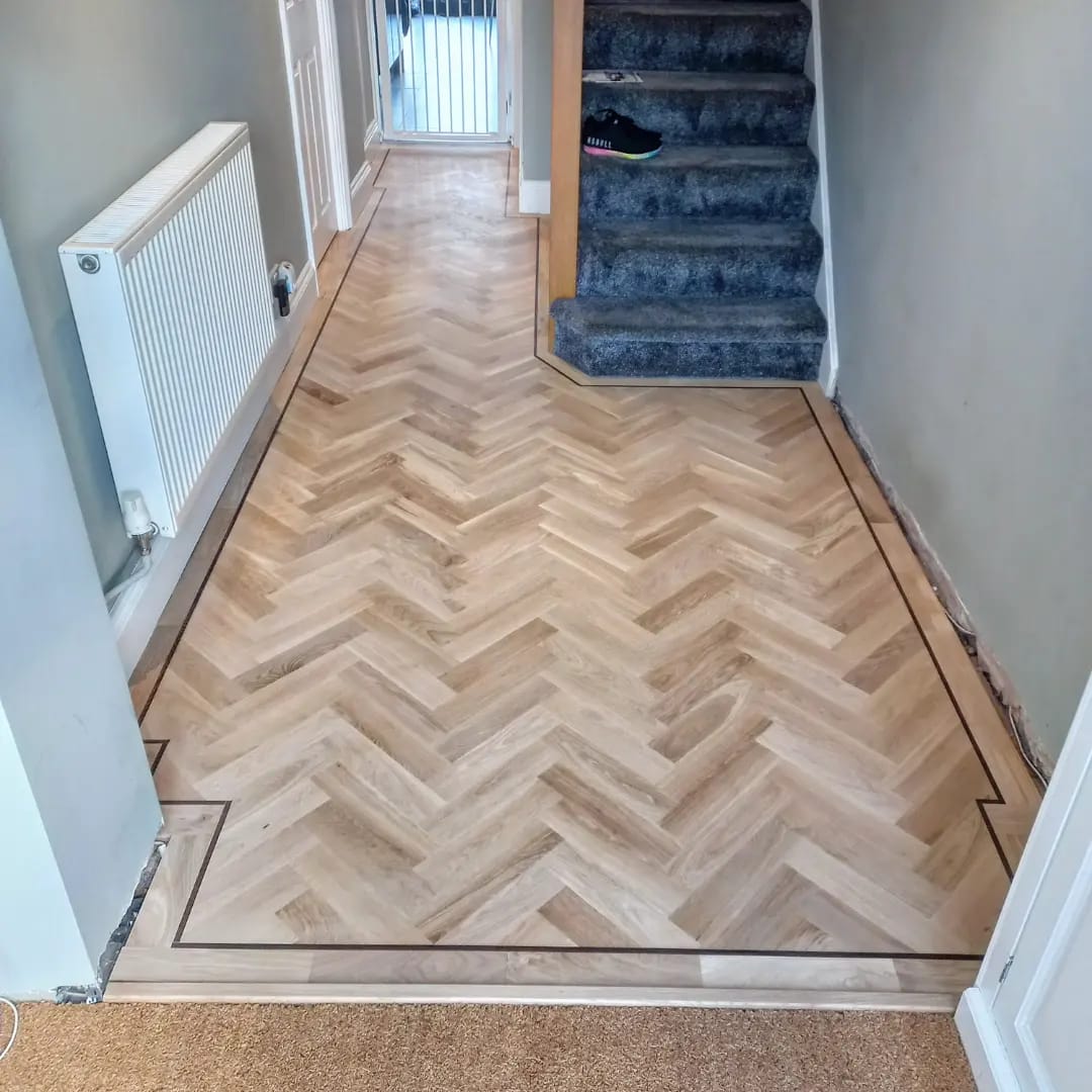 Light oak herringbone hallway floor with a dark border strip, running to the foot of the stairs