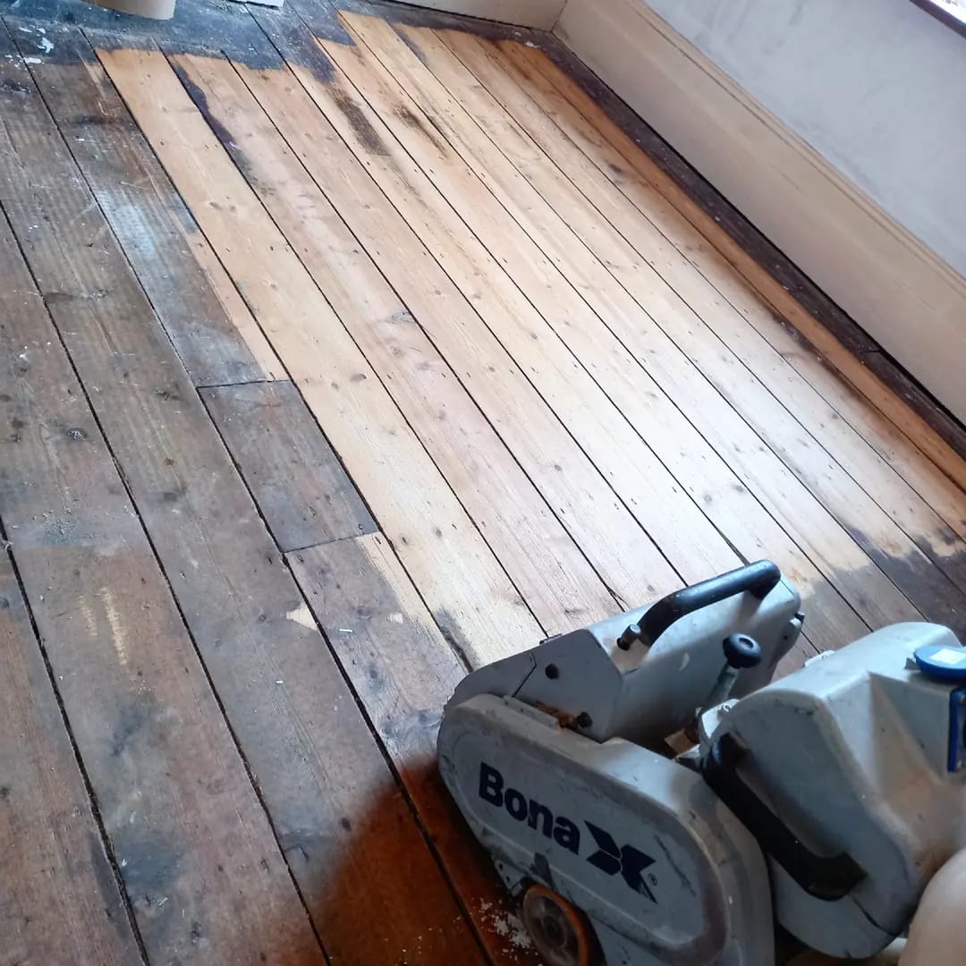Old pine floorboards part way through sanding, with a Bona sander in the foreground