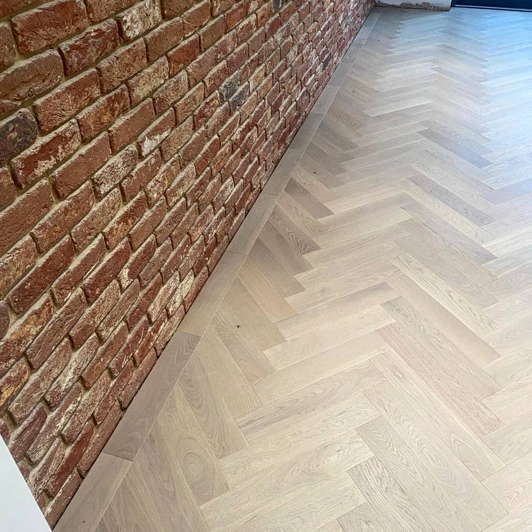 Pale oak herringbone floor running along an exposed red-brick wall