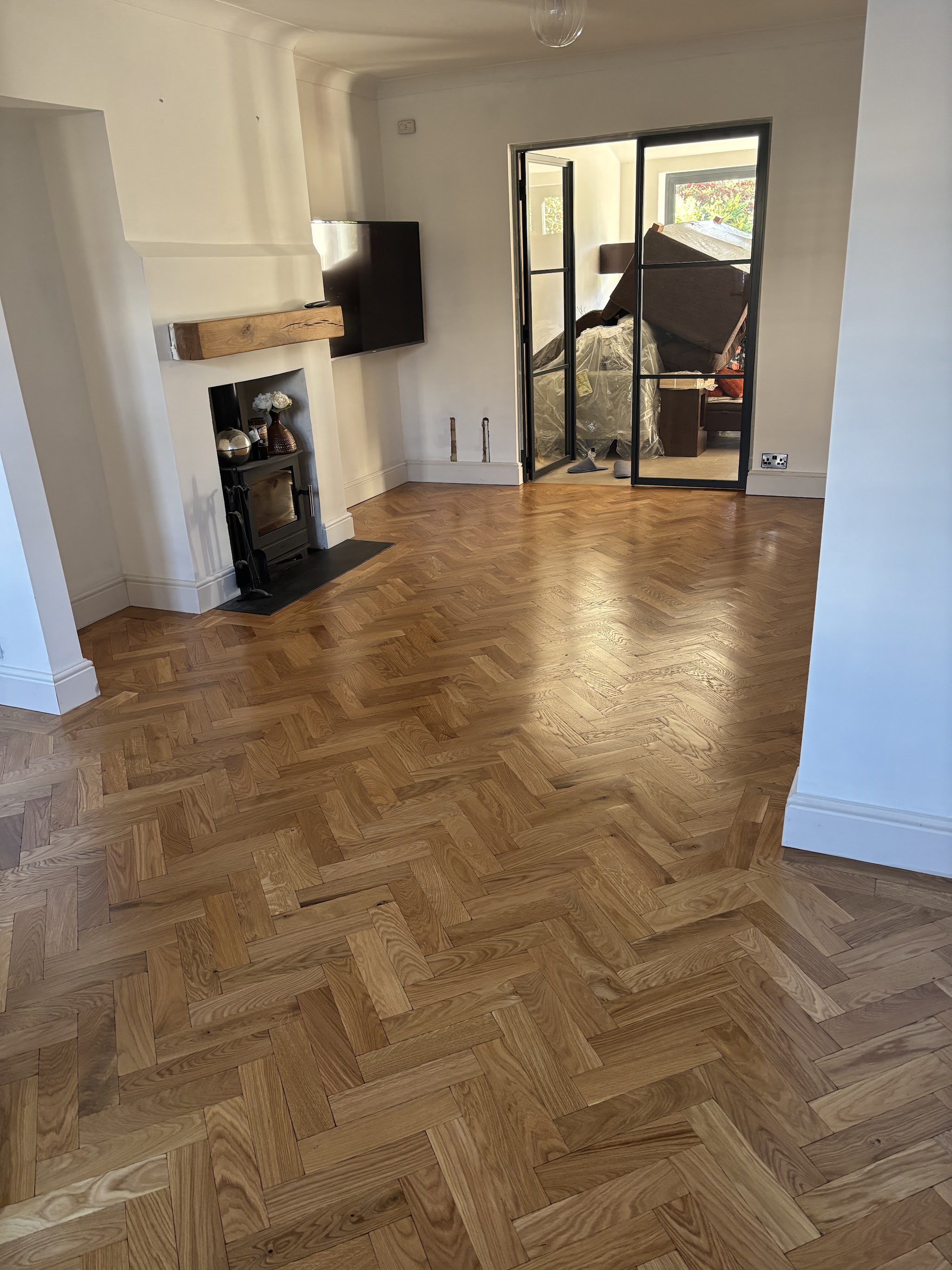 A finished mid-tone oak herringbone through-lounge with a log burner and glazed doors, photographed by the customer