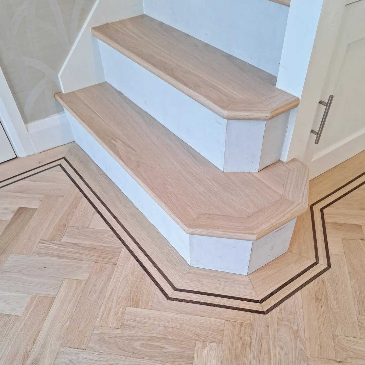 Oak-clad stair treads with rounded nosings above a herringbone floor edged with a dark border that follows the shape of the stairs