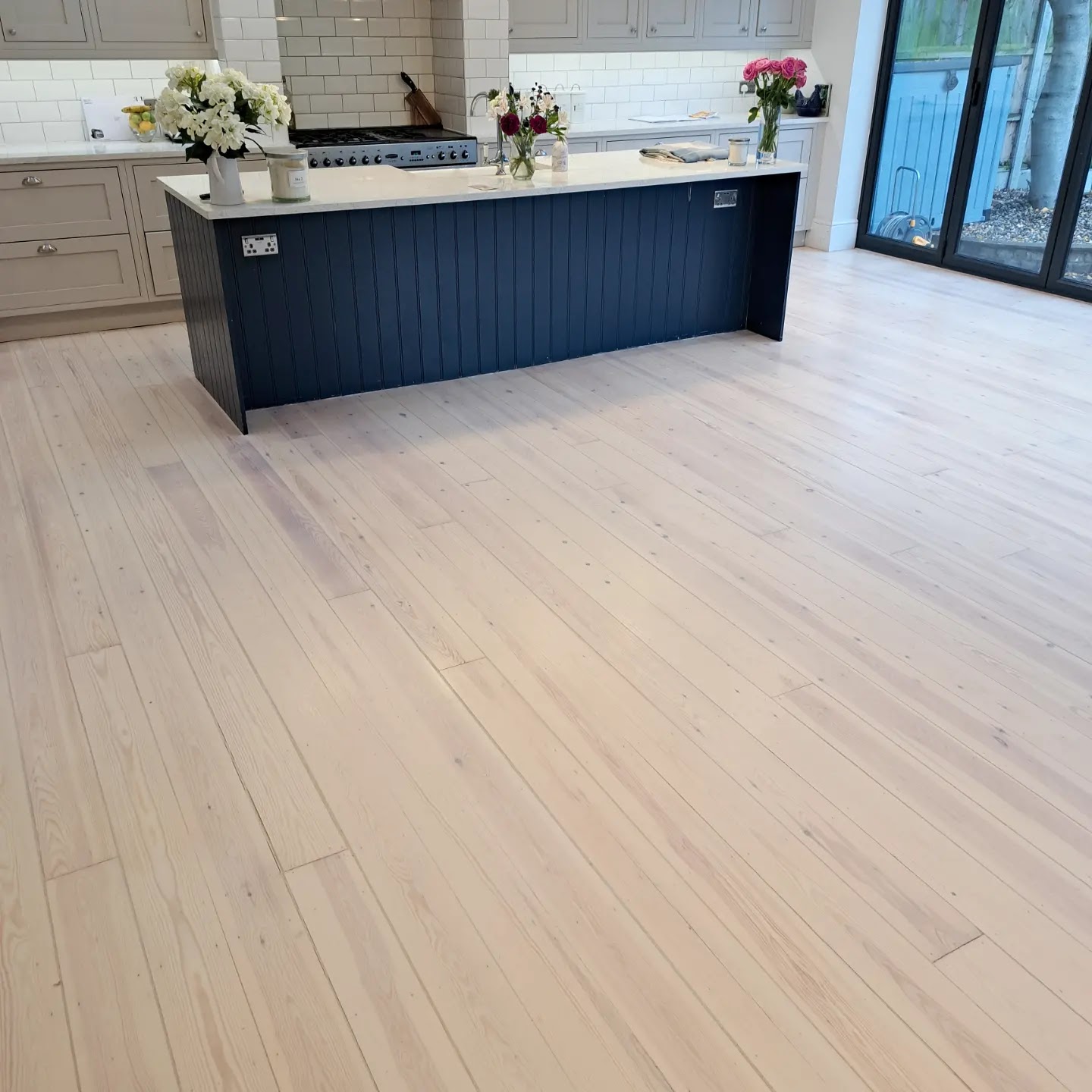 Large open-plan kitchen with a pale whitewashed plank floor, a navy island and bifold doors