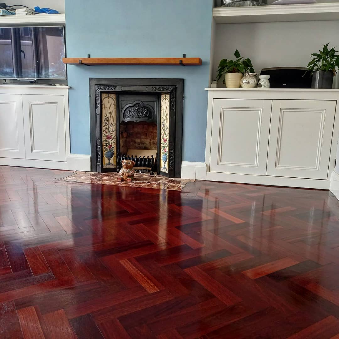 A high-gloss dark red herringbone parquet floor in a period living room with a cast-iron fireplace